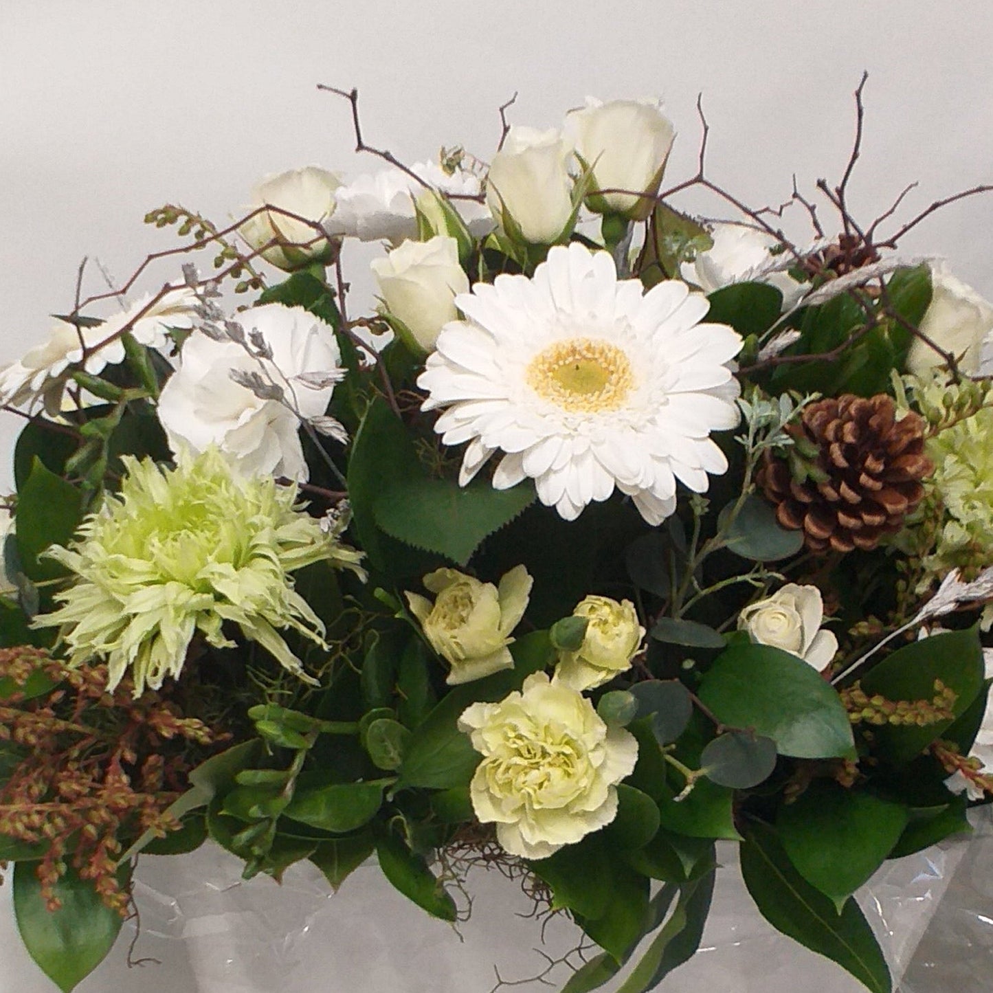 Floral arrangement with white gerberas, mini roses and green chrysies, carnations and cones