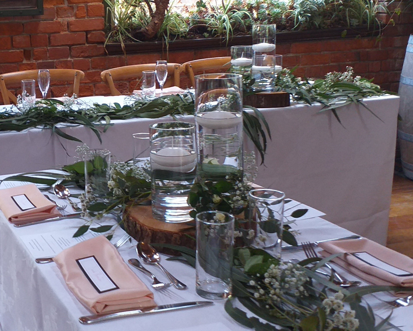 Table decoration in a central strip of gum leaves spray roses and gypsophilla combined with brides glass cylinder vases with floating candles