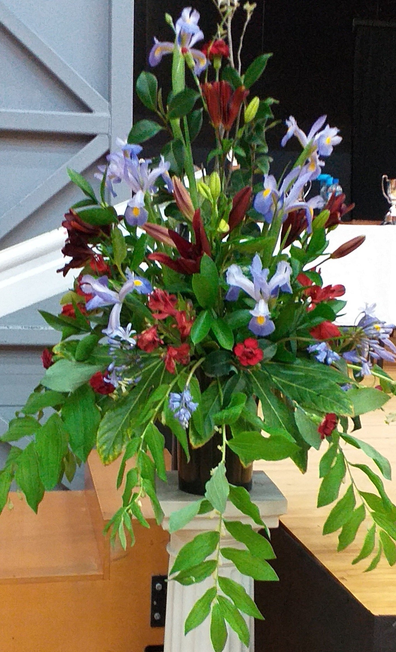 Pedestal arrangement of pale blue and red flowers. Irises, alstromeria, red asiatic lilies, red leucodendrons, pale blue agapanthus and carnations