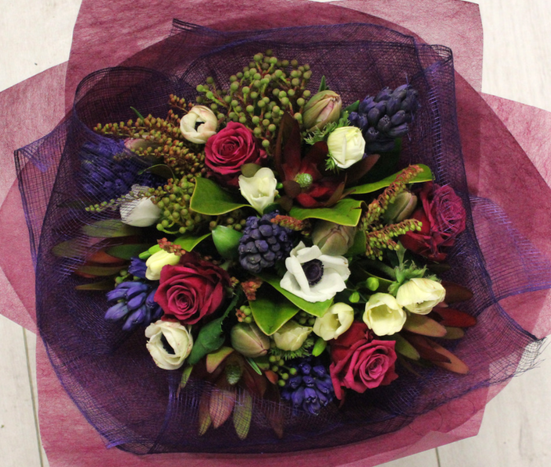 Bouquet of burgundy, hot pink, white and purple. Flowers include hot pink roses, leucadendron, sweet peas, anemone, freesias. Wrapped in burgundy and purple