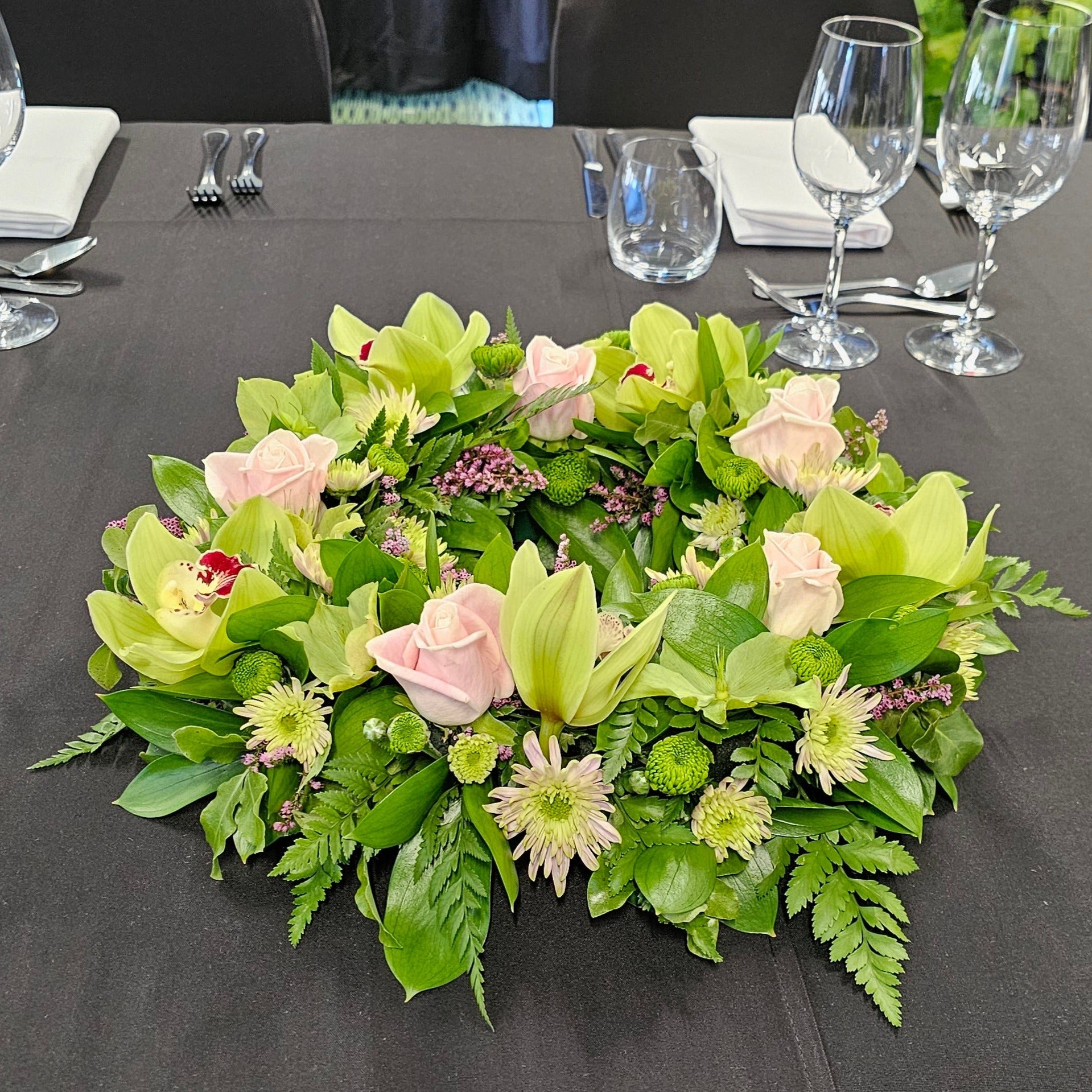 Table dcortion of wreath made from pink roses, greenorchids, green and pink chrysanthemums