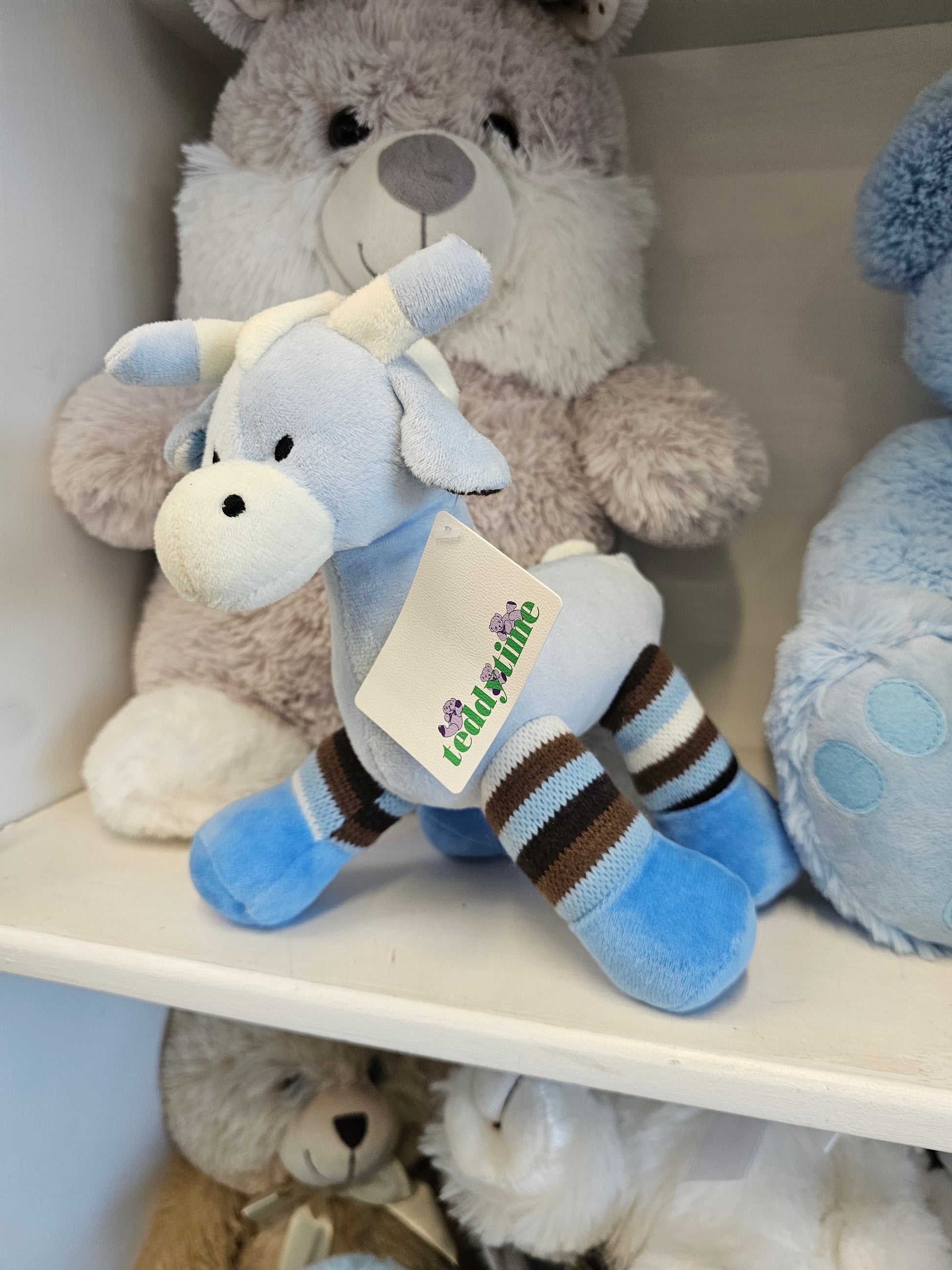 A plush toy cow with a light blue body, white face and horns, and brown-and-white striped legs