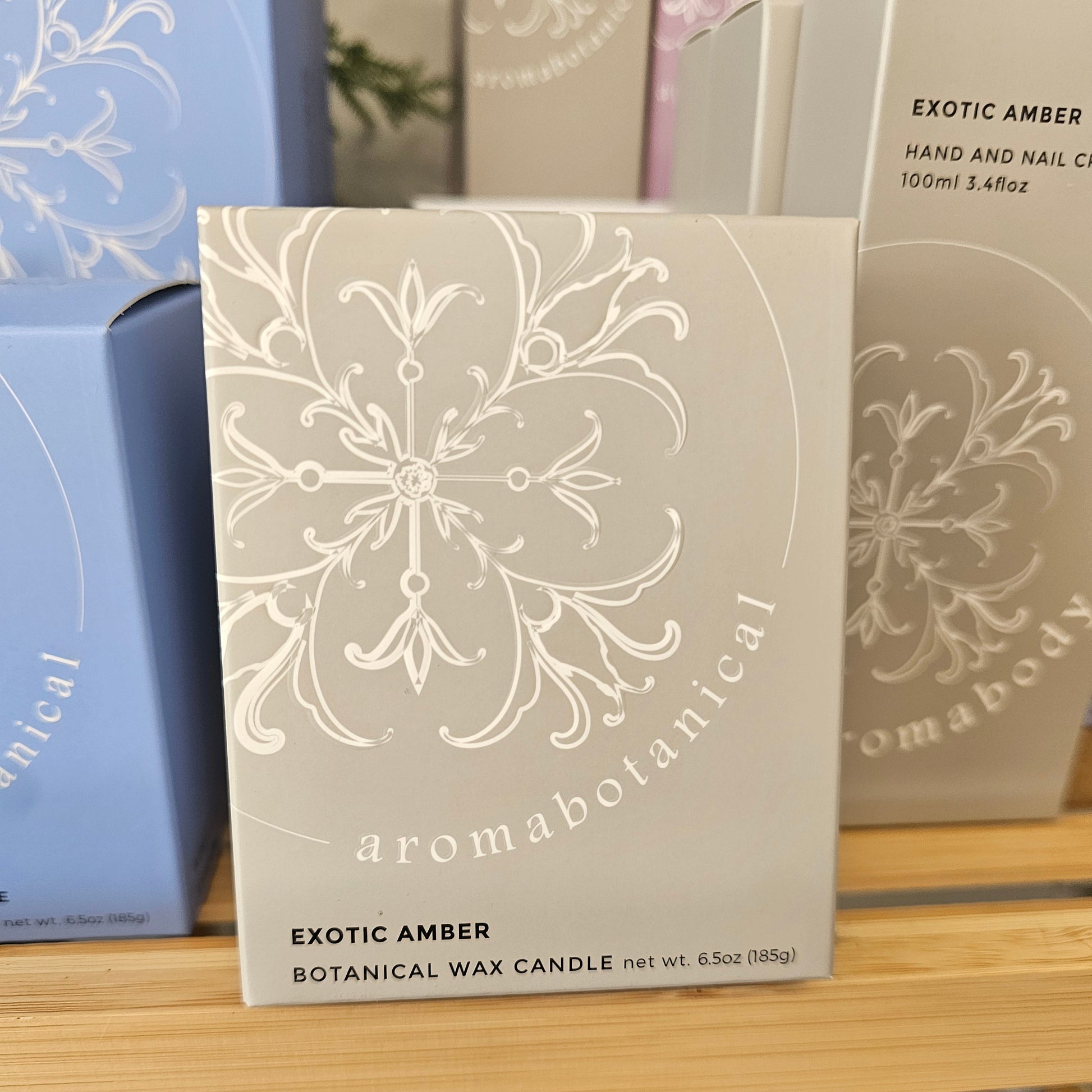 A boxed candle package labeled 'Exotic Amber Botanical Wax Candle' by Aromabotanical