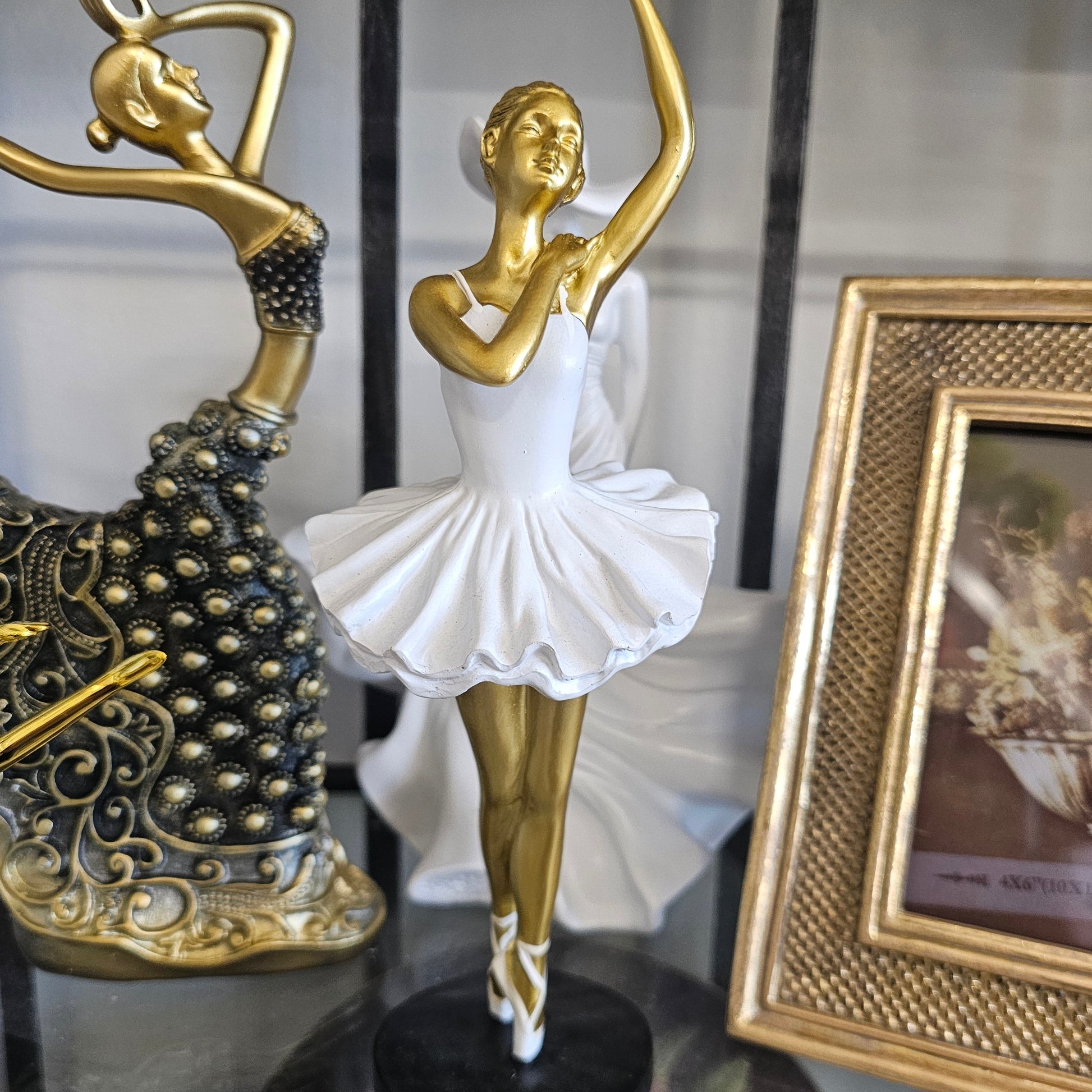 A decorative ballerina figurine in a white tutu with a gold arm and black base