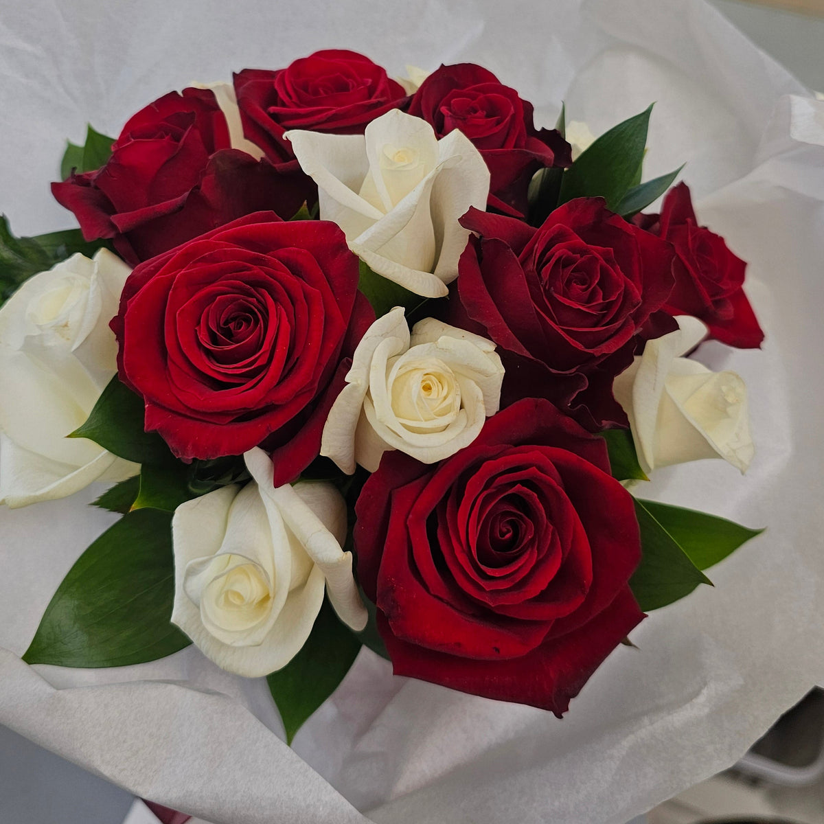A traditional bridal bouquet of mixed red and white roses with green leaves, wrapped in white tissue 