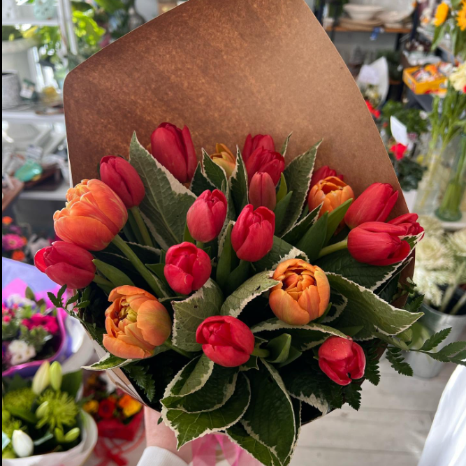 A bouquet of orange and red tulips wrapped in brown paper
