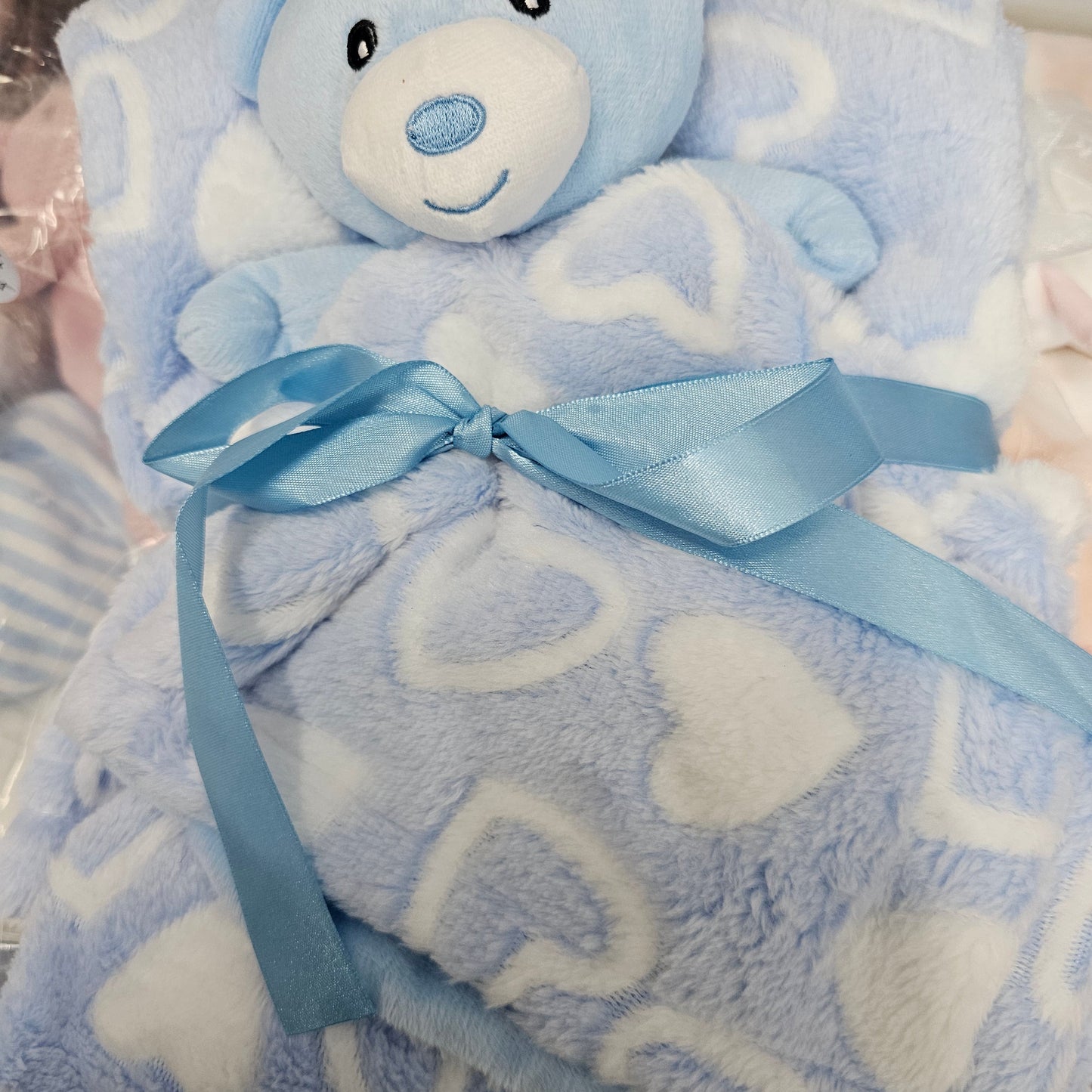 A baby gift set featuring a plush light blue bear toy and a matching fuzzy blanket with white heart patterns, tied with a light blue ribbon 