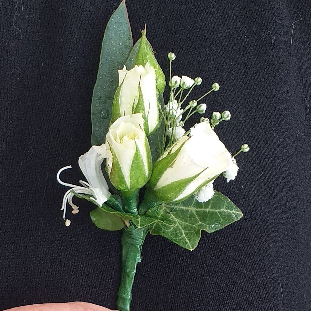 A white rose boutonniere with green leaves and stems