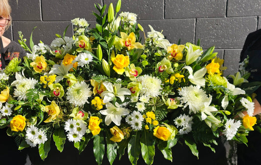 a very large casket spray in white chrysies lilies, green chrysies orchids, yellow roses chrysies orchids