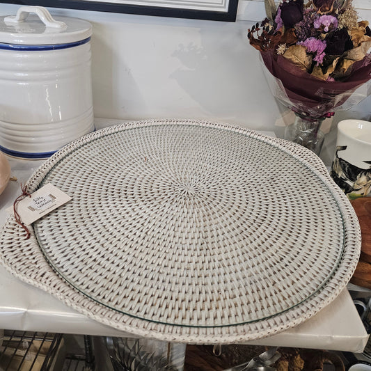 A glass tray with a round woven beige placemat with a concentric spiral pattern