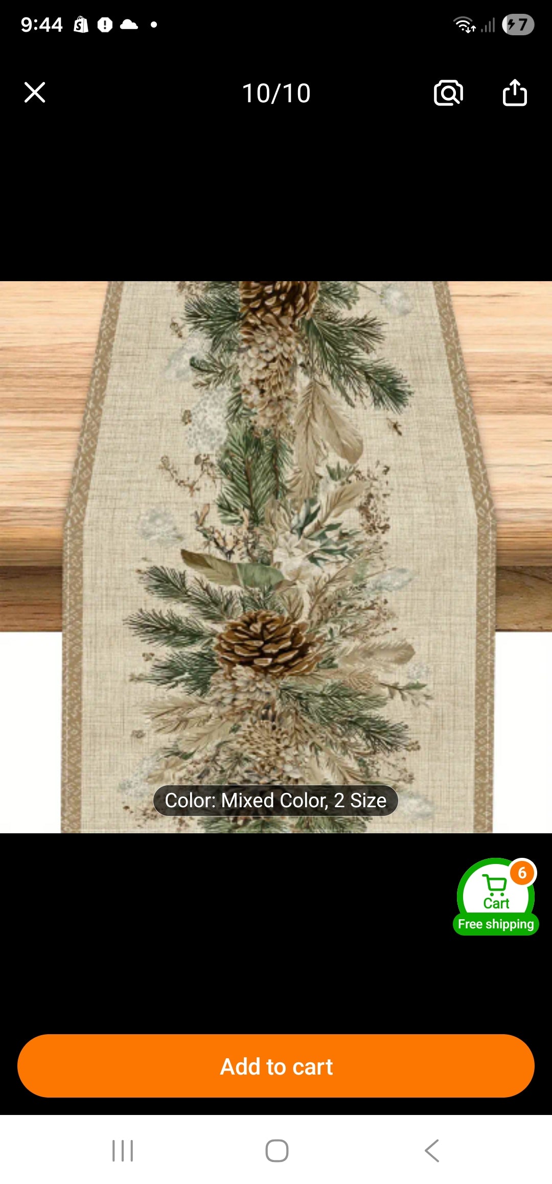 A rustic burlap table runner with a pinecone and evergreen branch pattern, shown on a wooden surface with a black mobile-commerce interface overlay.