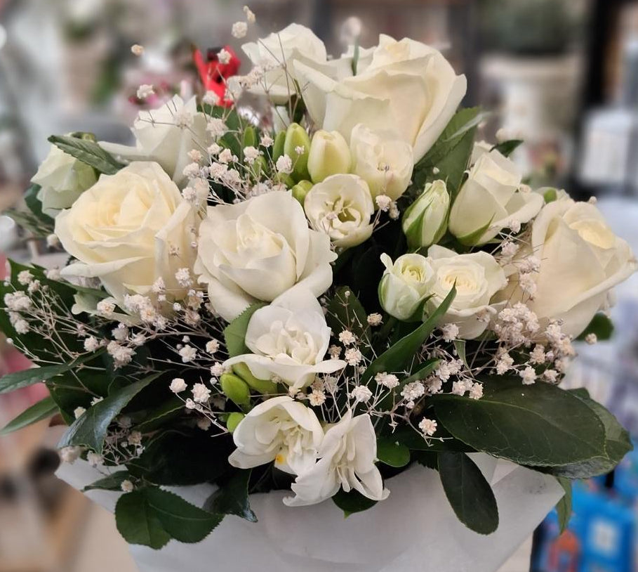 A bouquet of white roses, white alstro, gyp, white spray roses and green foliage wrapped in white tissue paper