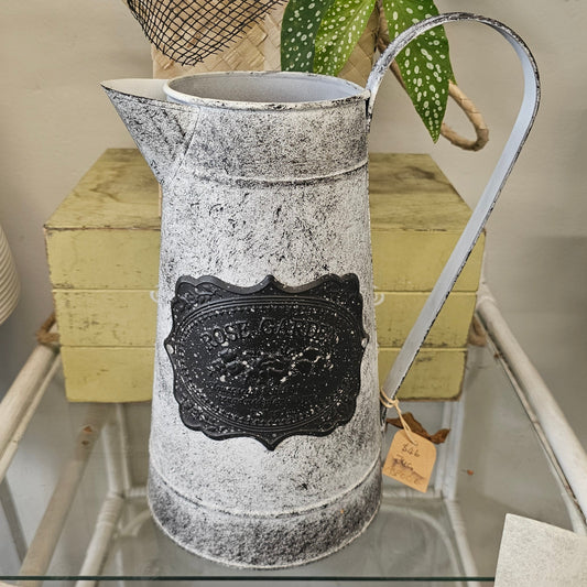 A distressed galvanized metal pitcher with a black decorative label on the front