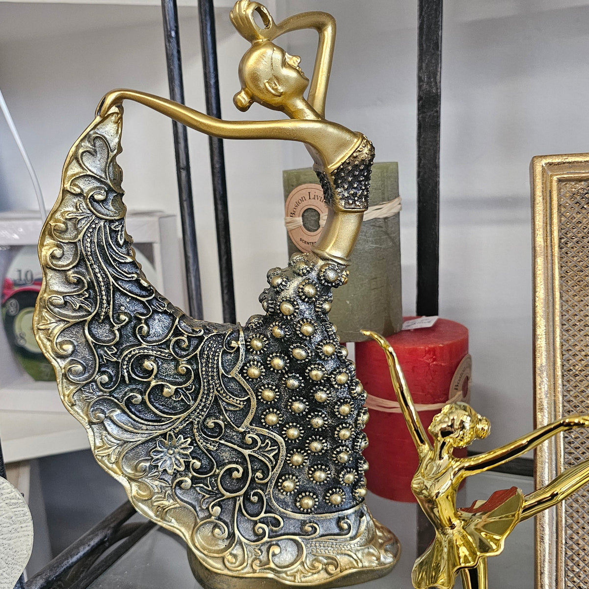 A decorative metal figurine of a classical dancer with an ornate, patterned skirt in gold tones,