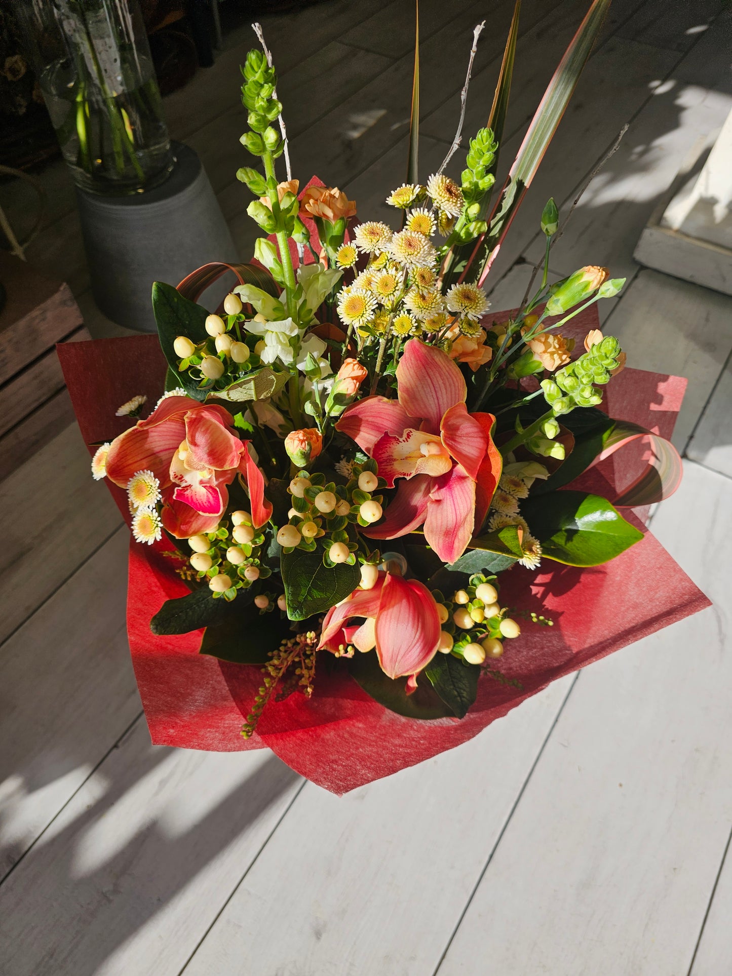 red cymbidium orchid with cream berries, mini white chrysies, and antirrinums wrapped in red vylene