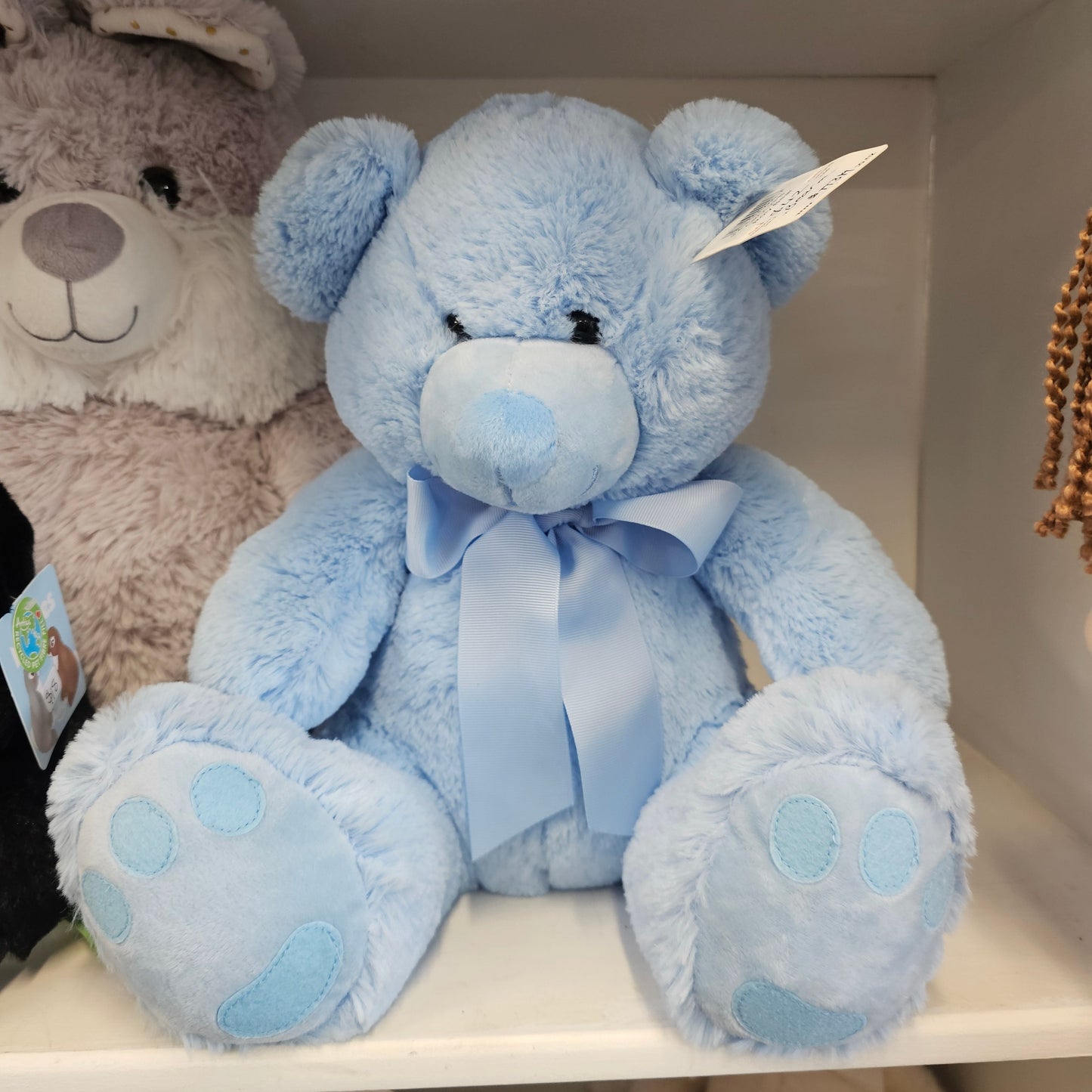 A light blue plush teddy bear with a matching blue satin bow and light blue paw pads