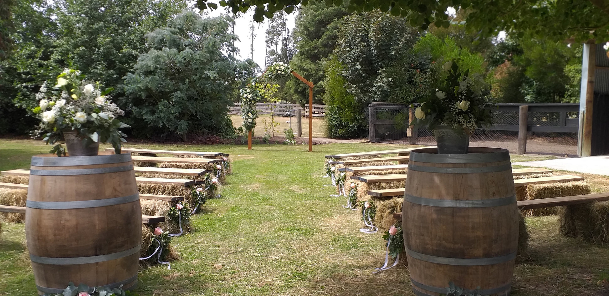 Garden setting with flower arrangements on barrels and an archway with decorations