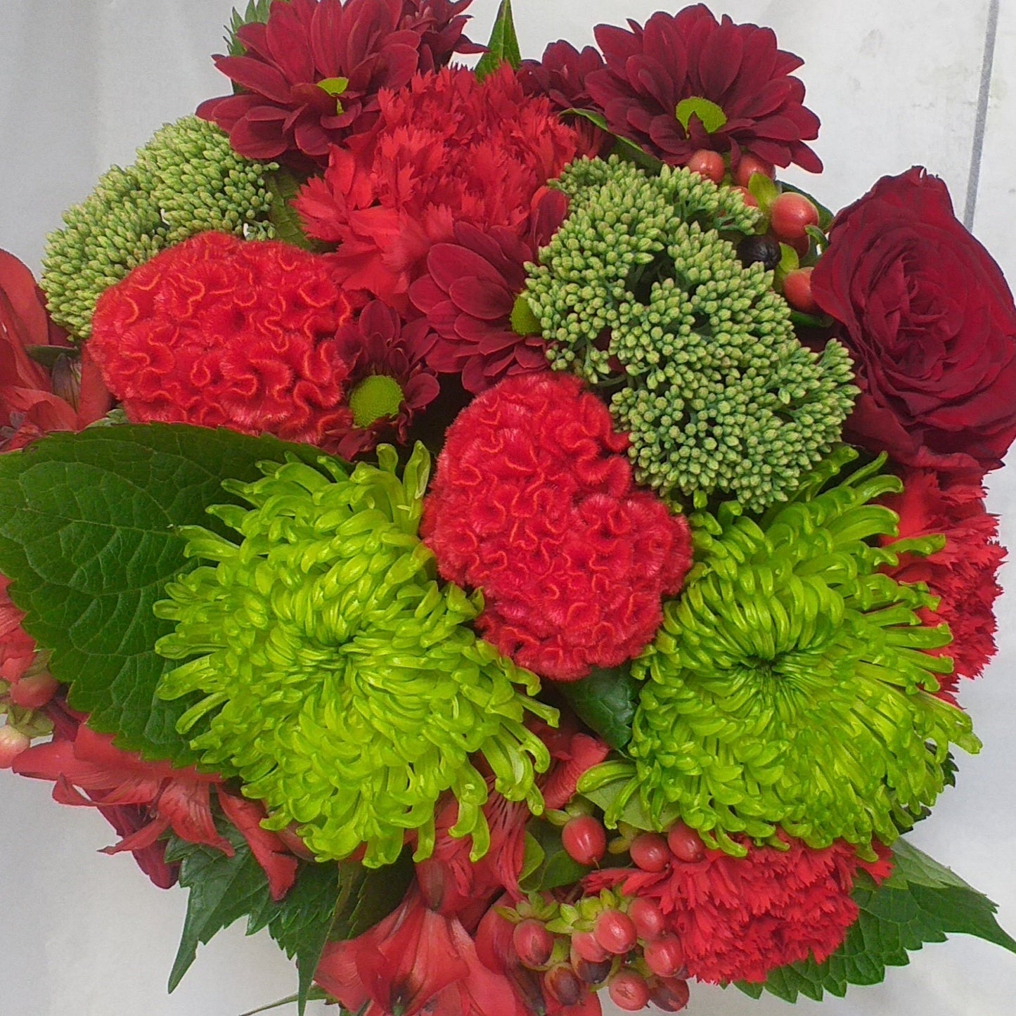Love Token arrangement of green chrysies and sedum, red roses, celosia, carnations, berries in a pot.