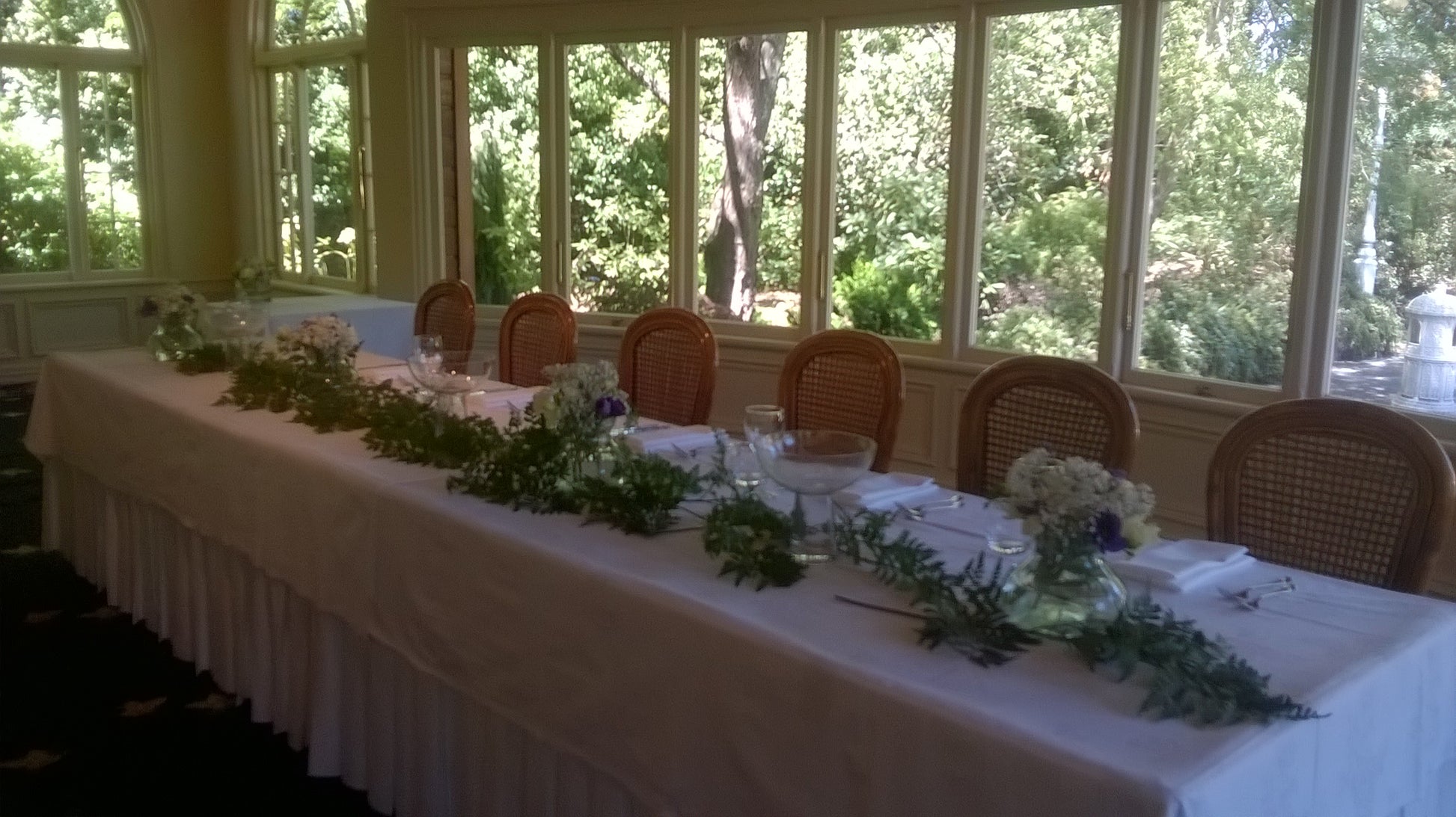 Table decoration, gypsophila, white rose, blue anenome posies in a fishbowl with leather fern laid along the table