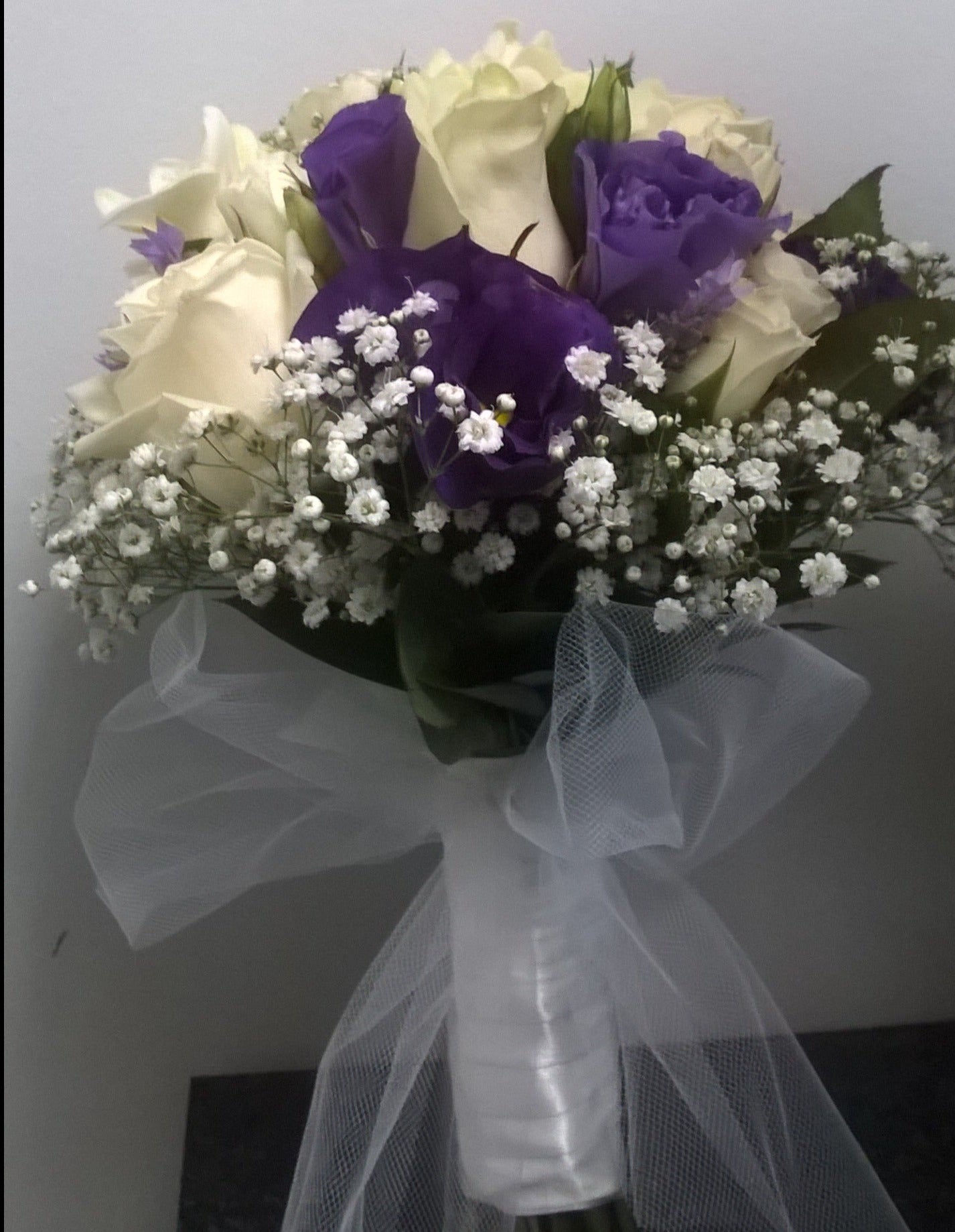 Bridal bouquet made with white roses, blue anenome, gypsophila and tied with a white satin ribbon with a tulle bow