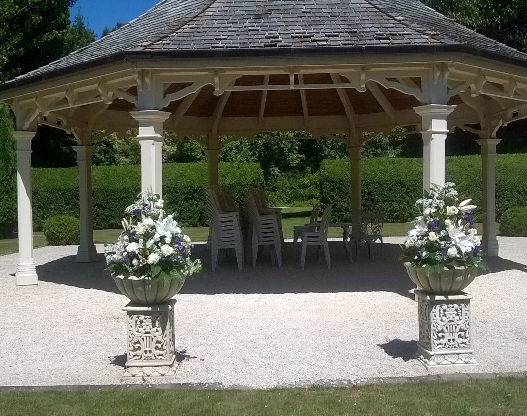 Pedestal garden arrangement in a scalloped bowl, with white roses, while lilies, white carnations, blue iris, blue anenome and gypsophilla