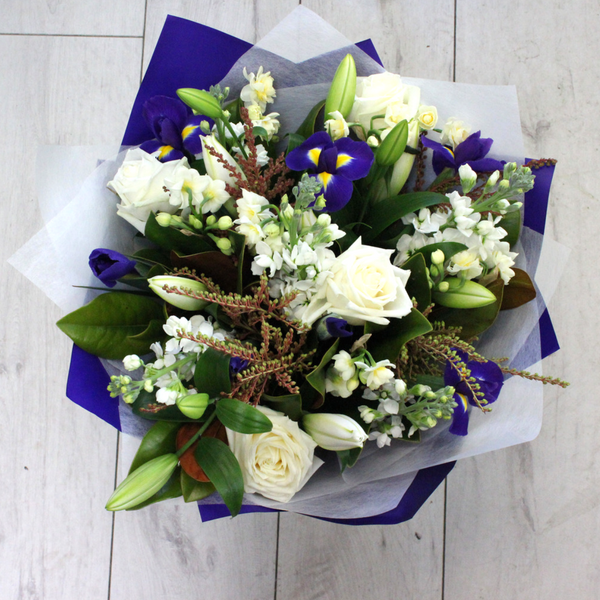 Blue and white flower bouquet. White roses, blue and yellow iris, early cheer, white stock, white lily. Wrapped in beautiful blue and white