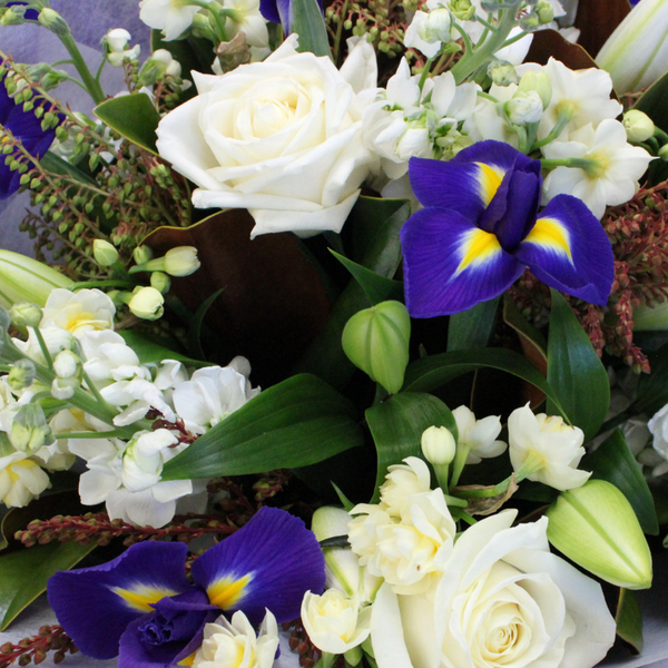 Blue and white flower bouquet. White roses, blue and yellow iris, early cheer, white stock, white lily. Wrapped in beautiful blue and white