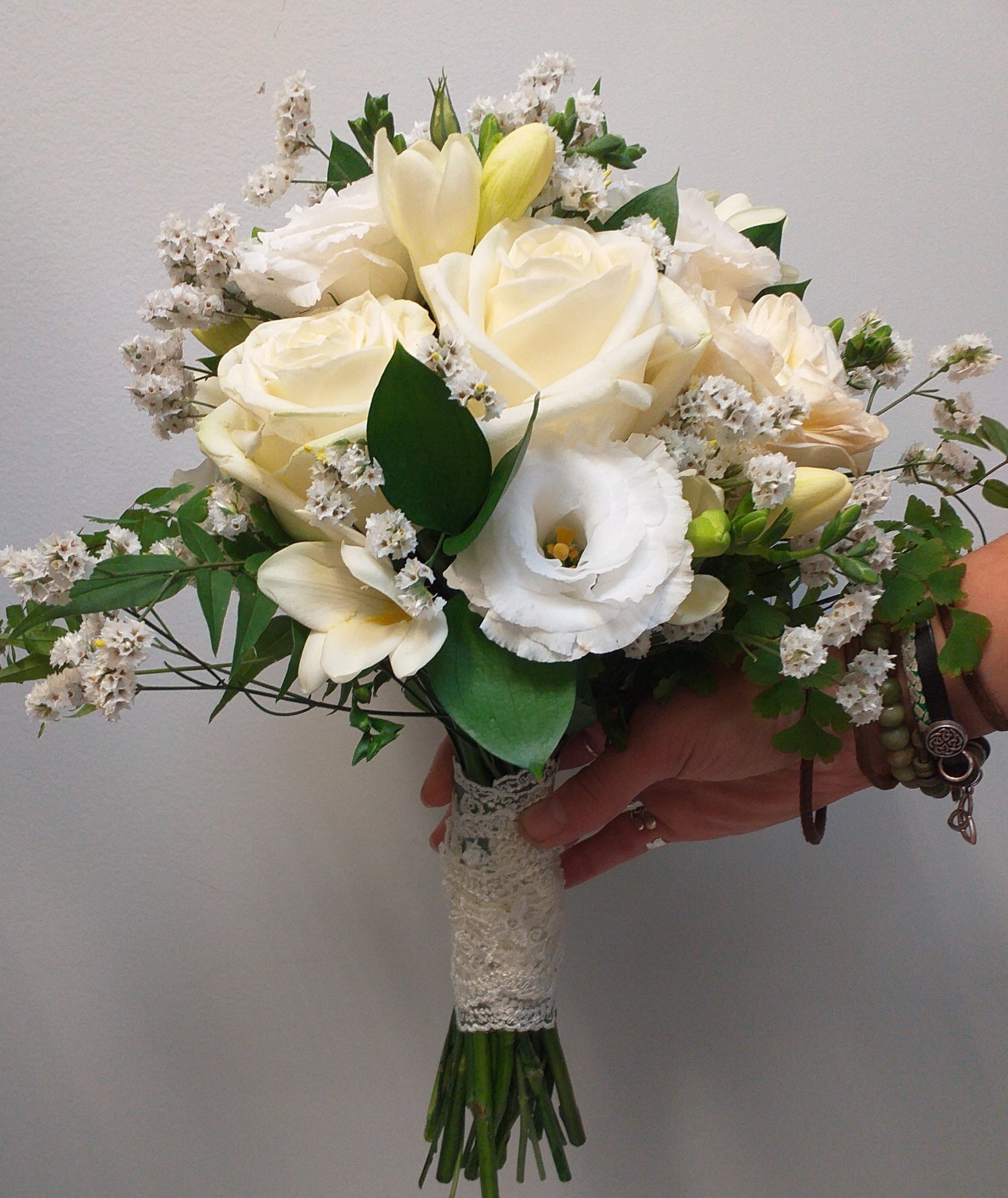 Bridal bouquet of cream roses, white freesias, white lisianthus and limonium tied with cream lace to match brides gown